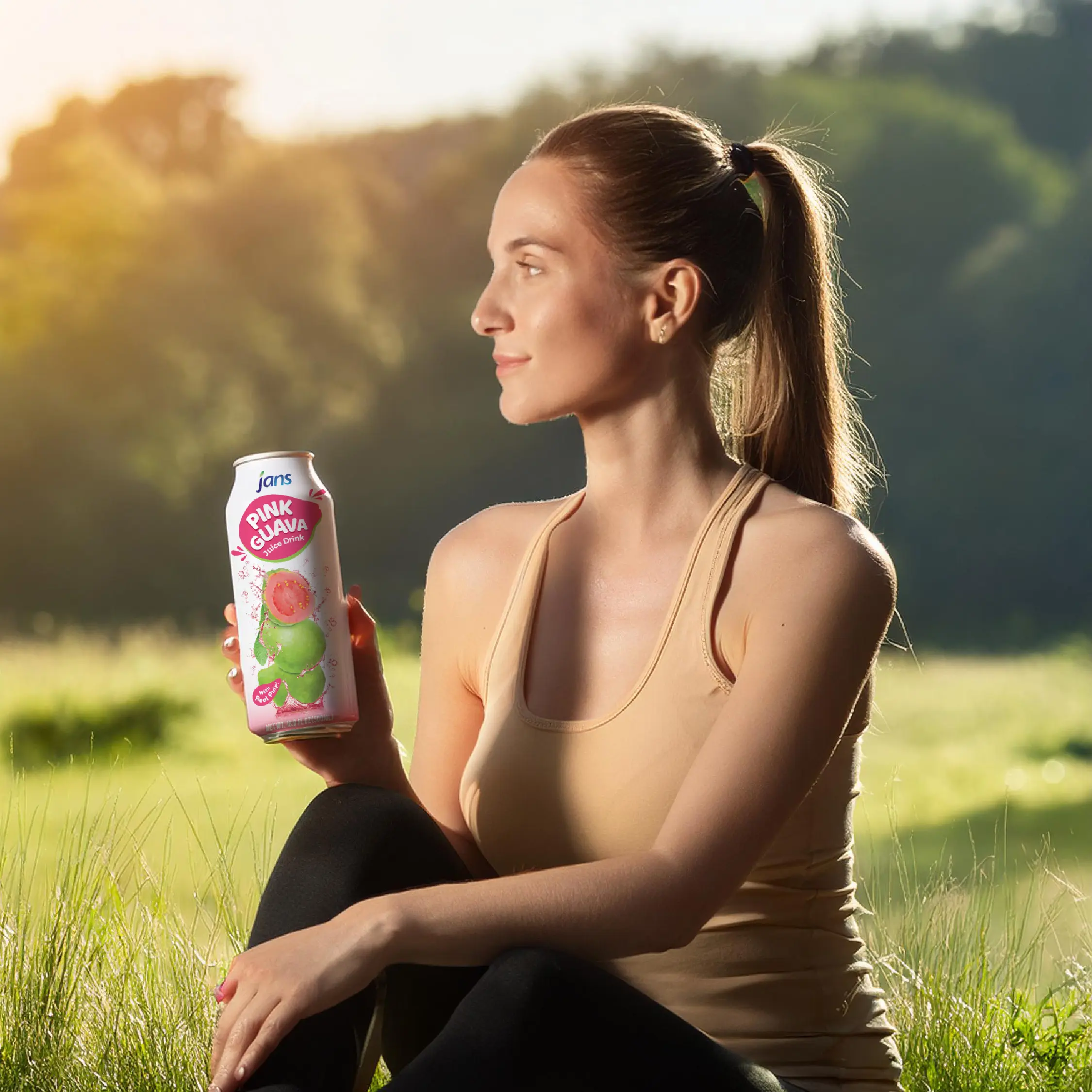 A woman sitting outdoors holding a can of Jans Pink Guava Juice Drink in natural light with a serene forest background